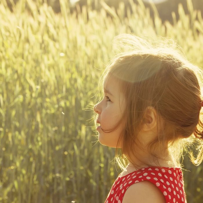 En lille pige ses i profil, stående på en eng.