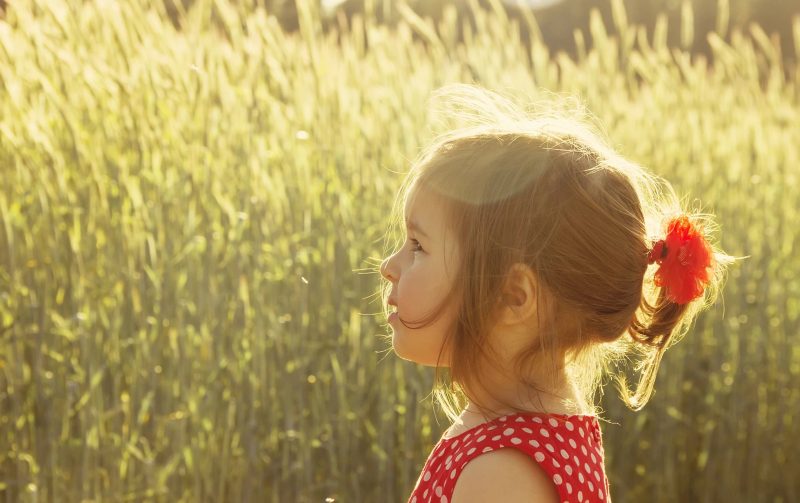 En lille pige ses i profil, stående på en eng.